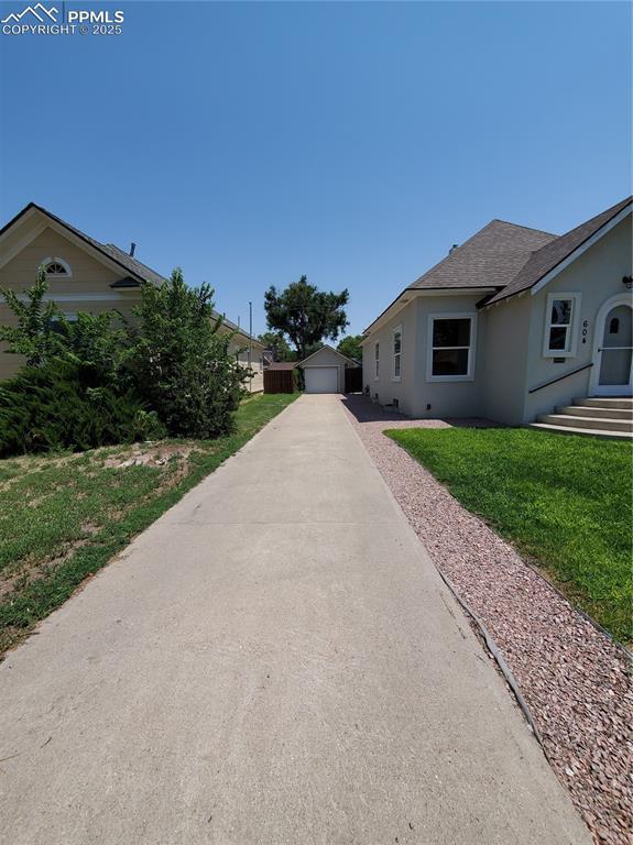 view of front of property featuring roof with shingles, a front yard, an outbuilding, a detached garage, and stucco siding
