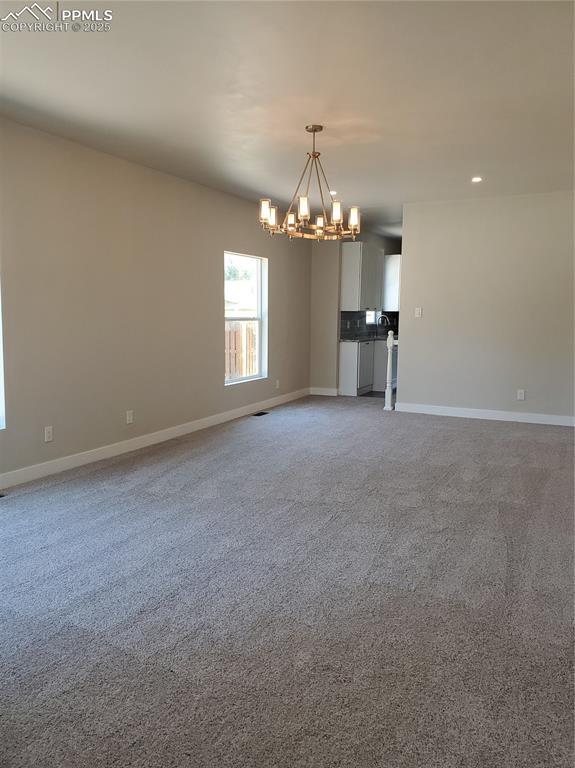 unfurnished room featuring baseboards, a notable chandelier, and light colored carpet