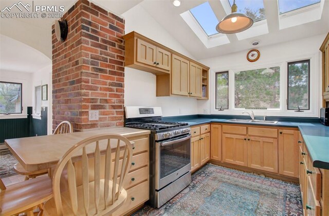 kitchen featuring a sink, light brown cabinets, gas range, and vaulted ceiling with skylight