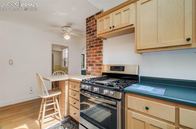 kitchen with light wood-style floors, gas range, ceiling fan, and light brown cabinetry