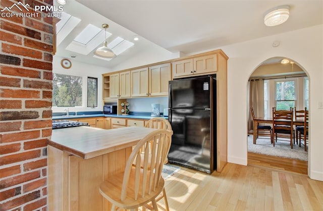 kitchen featuring freestanding refrigerator, light brown cabinets, light wood-type flooring, and a healthy amount of sunlight