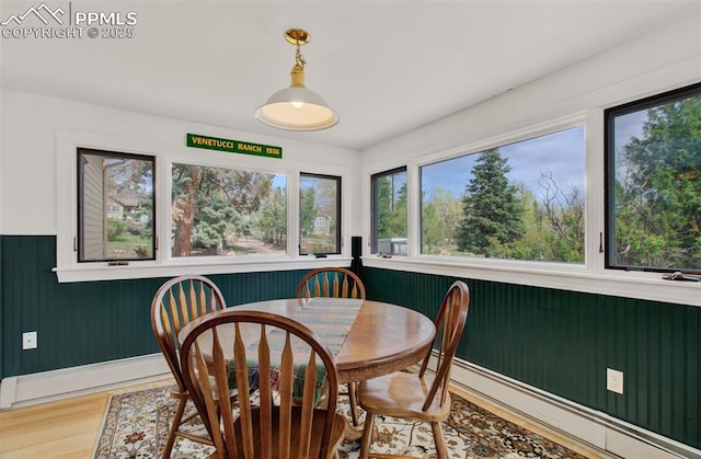 dining room featuring light wood-style floors, wooden walls, and a baseboard heating unit