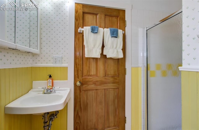bathroom featuring a stall shower, wainscoting, a sink, and wallpapered walls