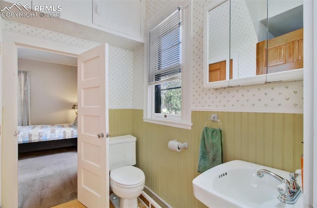 ensuite bathroom with wallpapered walls, toilet, ensuite bathroom, wainscoting, and a sink