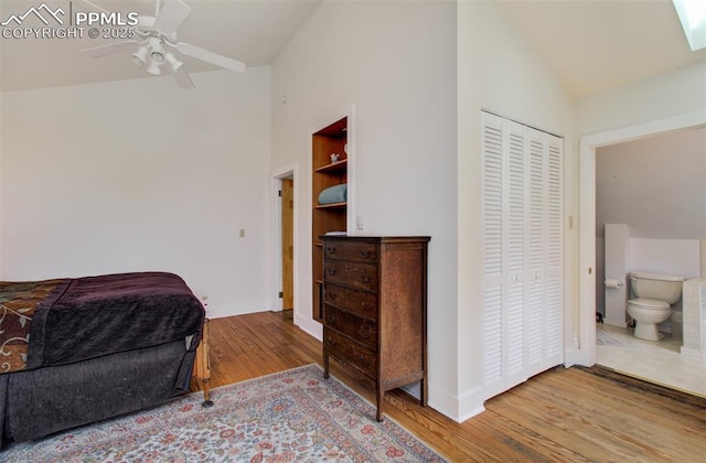 bedroom with a closet, baseboards, ensuite bath, vaulted ceiling, and wood finished floors