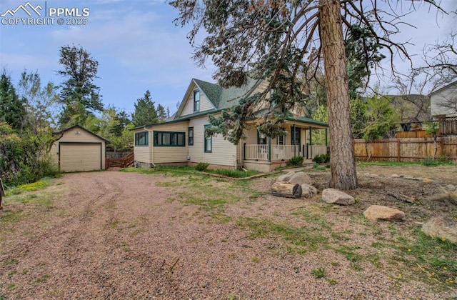 view of front facade with covered porch, a garage, dirt driveway, fence, and an outbuilding