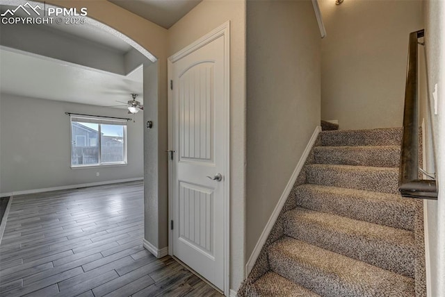 staircase featuring baseboards, arched walkways, ceiling fan, and wood finished floors