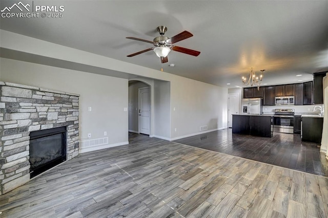 unfurnished living room with ceiling fan with notable chandelier, a sink, a fireplace, dark wood-style flooring, and arched walkways