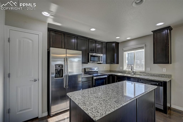 kitchen featuring light stone countertops, dark wood-type flooring, a sink, a kitchen island, and stainless steel appliances