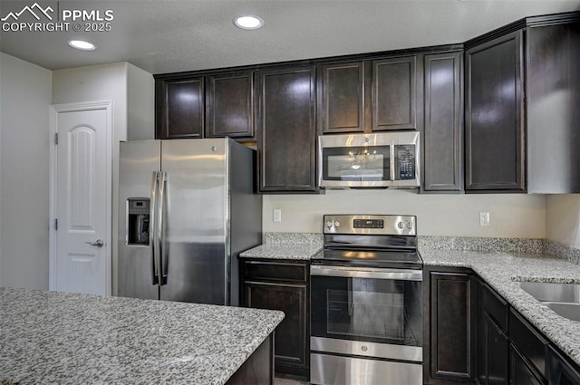 kitchen featuring dark brown cabinetry, appliances with stainless steel finishes, light stone countertops, and recessed lighting