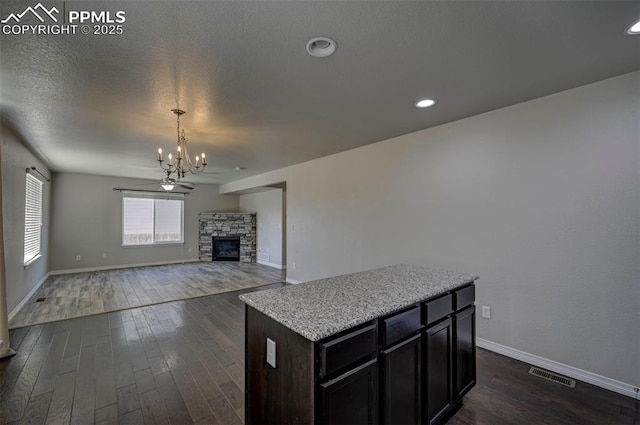 unfurnished living room with visible vents, a fireplace, a chandelier, dark wood-style floors, and baseboards