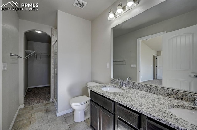 bathroom featuring toilet, a spacious closet, visible vents, and a sink