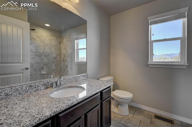 bathroom with baseboards, toilet, visible vents, tiled shower, and vanity