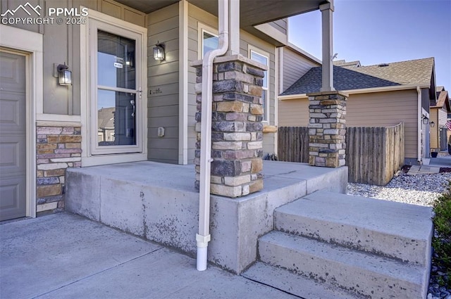 entrance to property featuring covered porch, roof with shingles, and stone siding
