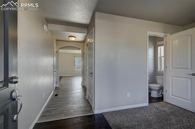 hall with a textured ceiling, dark wood-style flooring, baseboards, and arched walkways
