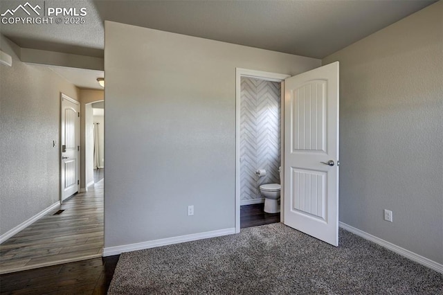 unfurnished bedroom featuring ensuite bath, dark wood-type flooring, and baseboards