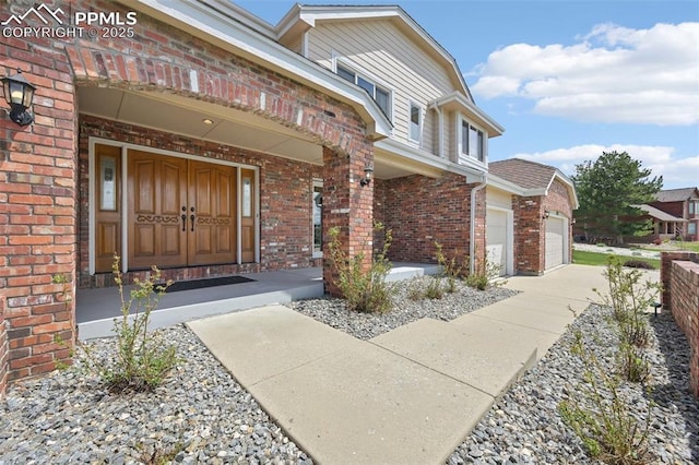 entrance to property with brick siding, a garage, driveway, and covered porch