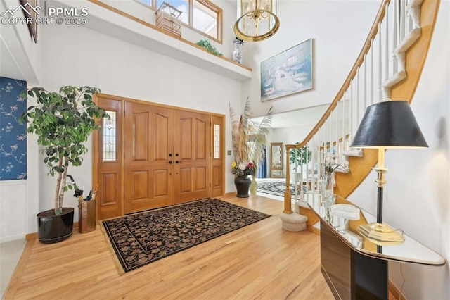 foyer entrance with wood finished floors, stairway, a towering ceiling, wallpapered walls, and wainscoting