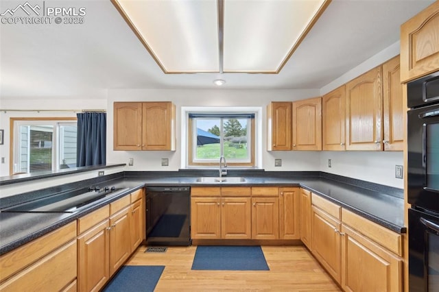 kitchen featuring black appliances, a sink, dark countertops, and light wood-style flooring