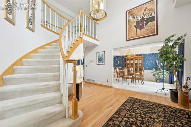 staircase with a chandelier, wood finished floors, a high ceiling, and baseboards