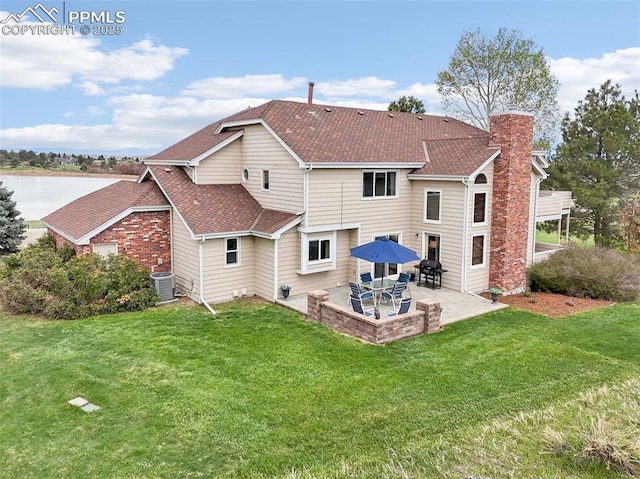rear view of house with central air condition unit, a patio area, a chimney, a yard, and roof with shingles