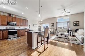 10150 Bracknell Pl, Peyton, CO 80831 - kitchen featuring stainless steel appliances, wood finished floors, decorative light fixtures, a kitchen breakfast bar, and a kitchen island with sink