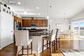10150 Bracknell Pl, Peyton, CO 80831 - kitchen featuring stainless steel microwave, brown cabinets, range, dark wood-type flooring, and a breakfast bar