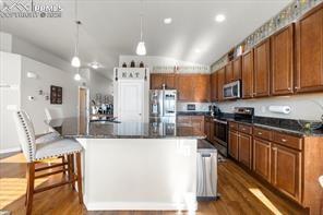 10150 Bracknell Pl, Peyton, CO 80831 - kitchen featuring stainless steel appliances, dark countertops, wood finished floors, a large island, and brown cabinets
