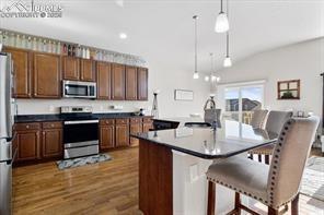 10150 Bracknell Pl, Peyton, CO 80831 - kitchen with appliances with stainless steel finishes, dark wood-style flooring, hanging light fixtures, a kitchen bar, and an island with sink