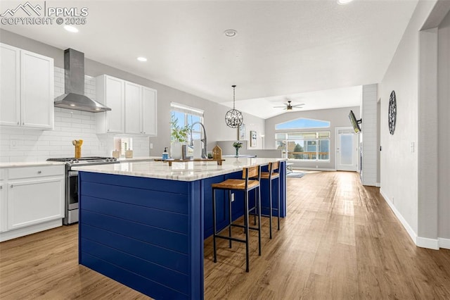 12383 Pine Valley Cir, Peyton, CO 80831 - kitchen with stainless steel gas range oven, wall chimney exhaust hood, a center island with sink, light wood-style floors, and white cabinets