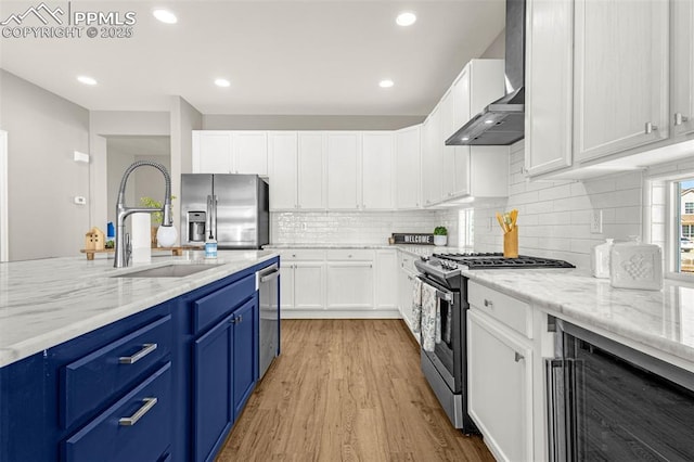 12383 Pine Valley Cir, Peyton, CO 80831 - kitchen with stainless steel appliances, blue cabinetry, wine cooler, a sink, and wall chimney range hood