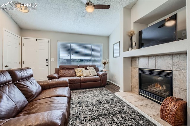 6640 Oakwood Blvd, Colorado Springs, CO 80923 - living room with a tiled fireplace, ceiling fan, a textured ceiling, wood finished floors, and baseboards