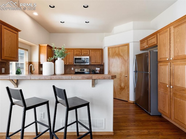 7049 Vasalias Hts, Colorado Springs, CO 80923 - kitchen with stainless steel appliances, tasteful backsplash, dark wood finished floors, and a kitchen bar