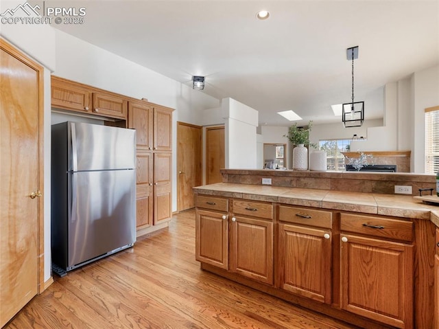 7049 Vasalias Hts, Colorado Springs, CO 80923 - kitchen featuring a skylight, brown cabinets, freestanding refrigerator, hanging light fixtures, and light wood-style floors