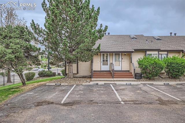 view of front of house featuring a porch, a shingled roof, fence, and uncovered parking