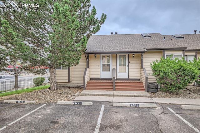 view of front of house featuring a porch, roof with shingles, fence, and uncovered parking