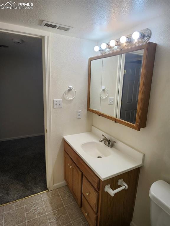 half bathroom with toilet, vanity, visible vents, and a textured ceiling