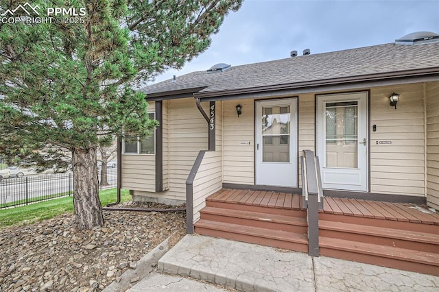 view of exterior entry with a porch, roof with shingles, and fence