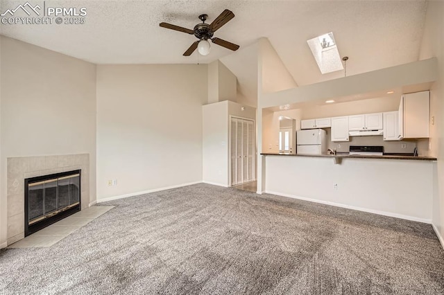 unfurnished living room with a ceiling fan, high vaulted ceiling, a fireplace, a skylight, and light carpet
