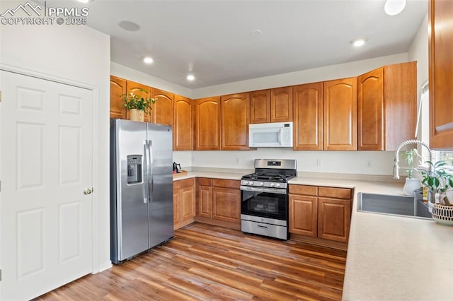 kitchen with stainless steel appliances, a sink, wood finished floors, brown cabinets, and light countertops