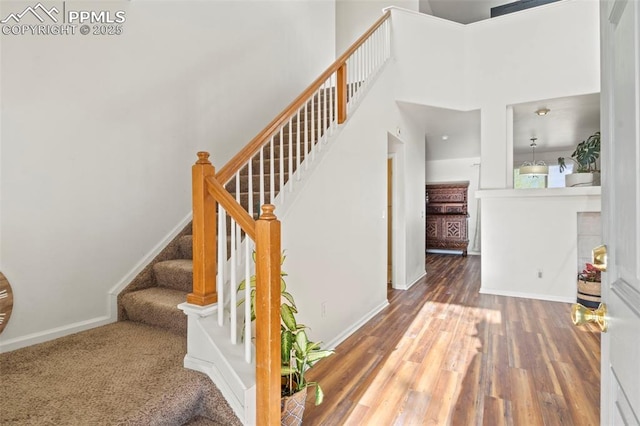 staircase with wood finished floors, baseboards, and a high ceiling