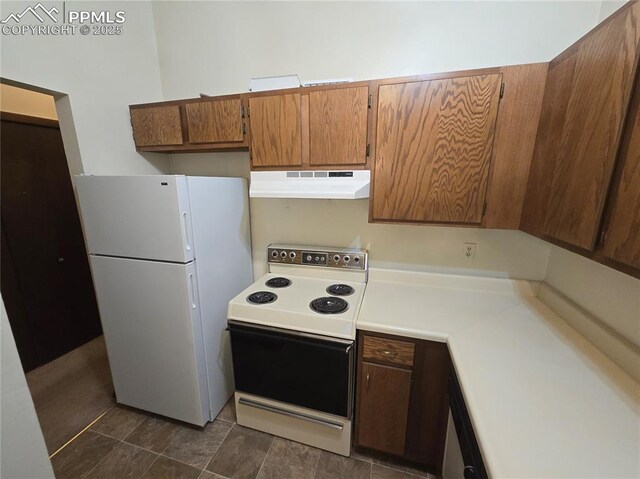 kitchen with freestanding refrigerator, brown cabinetry, electric range oven, under cabinet range hood, and light countertops
