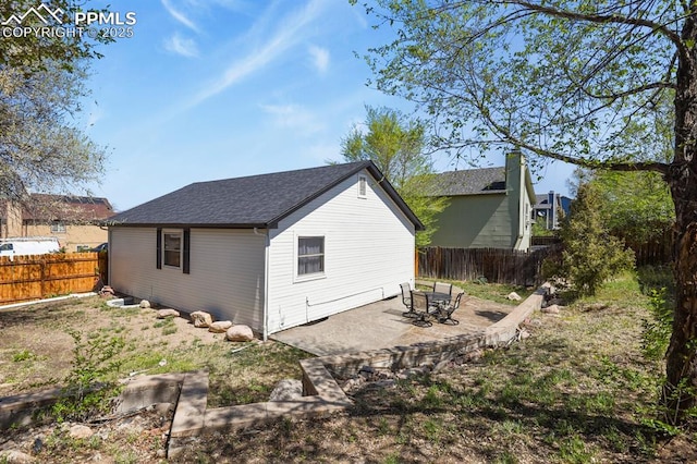 rear view of house featuring a patio, a shingled roof, and a fenced backyard
