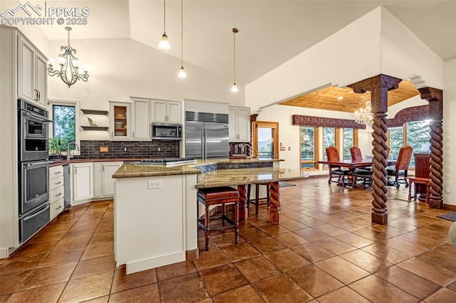 17995 Minglewood Trl, Monument, CO 80132 - kitchen with appliances with stainless steel finishes, a chandelier, decorative columns, a warming drawer, and high vaulted ceiling