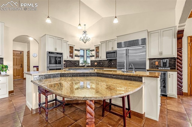 17995 Minglewood Trl, Monument, CO 80132 - kitchen with appliances with stainless steel finishes, a large island, a breakfast bar area, backsplash, and high vaulted ceiling