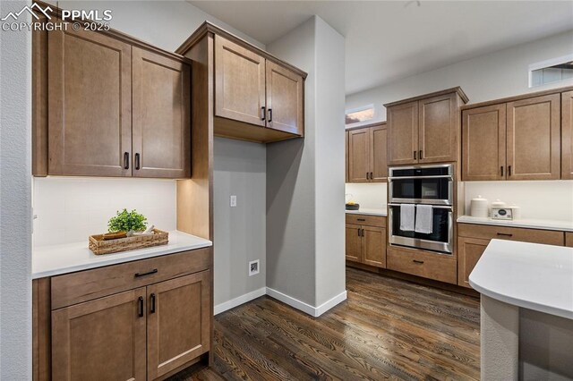kitchen with double oven, dark wood finished floors, light countertops, and baseboards