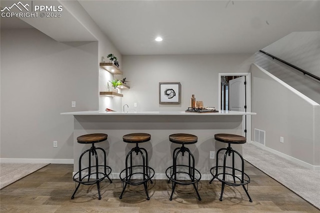 kitchen with wood finished floors, a breakfast bar area, a peninsula, baseboards, and recessed lighting