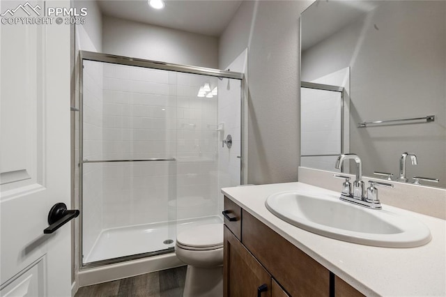bathroom featuring wood finished floors, a shower stall, toilet, and vanity