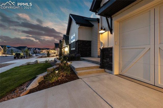 view of property exterior featuring stone siding, a residential view, board and batten siding, and concrete driveway