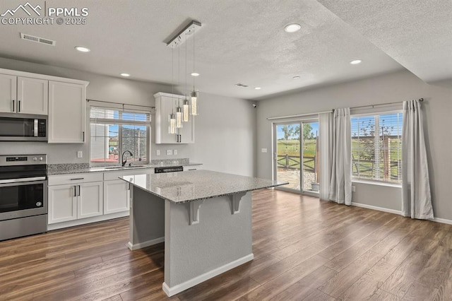 7238 Fauna Glen Dr, Colorado Springs, CO 80927 - kitchen featuring appliances with stainless steel finishes, a textured ceiling, white cabinetry, dark wood-type flooring, and a center island